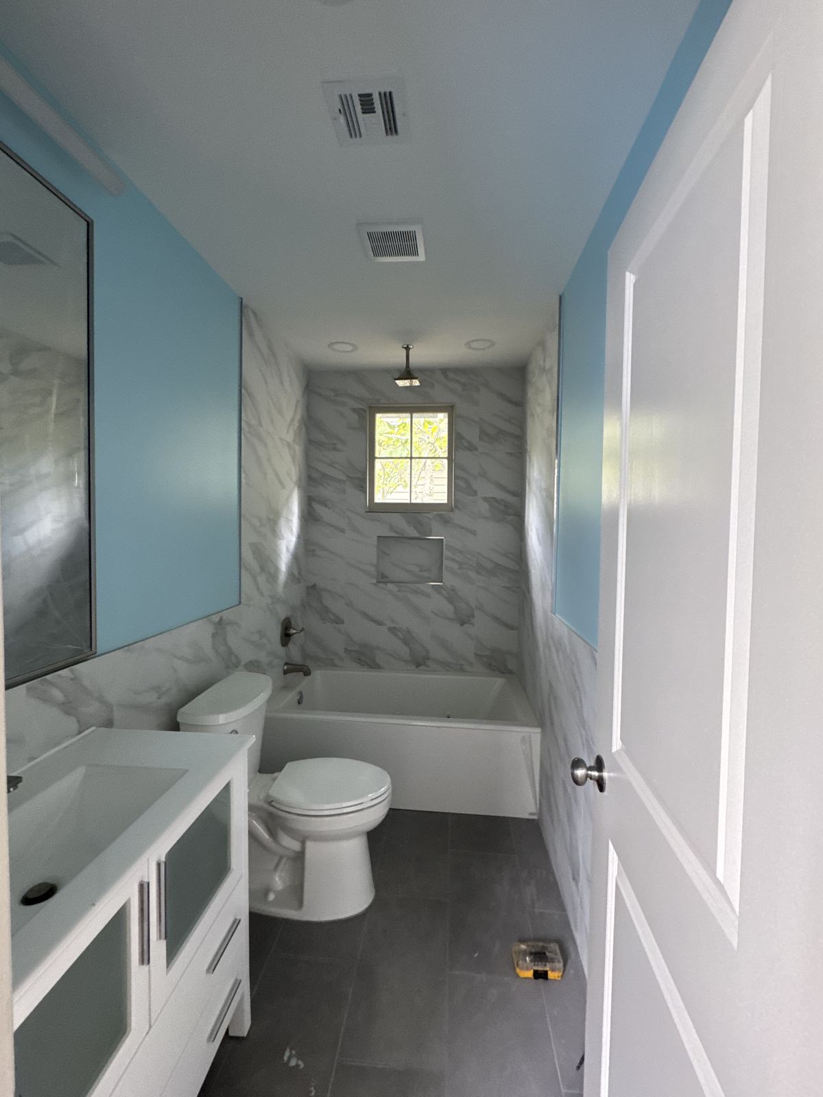 Blue bathroom with marble tub surround, ceiling rain head and matching marble walls