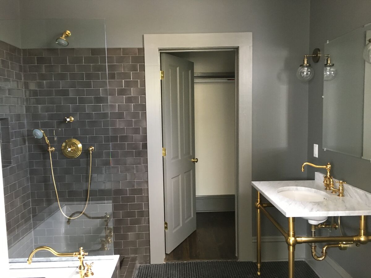 Charcoal subway tile bathroom with brass console vanity, marble top, gold shower fixtures, and globe sconces