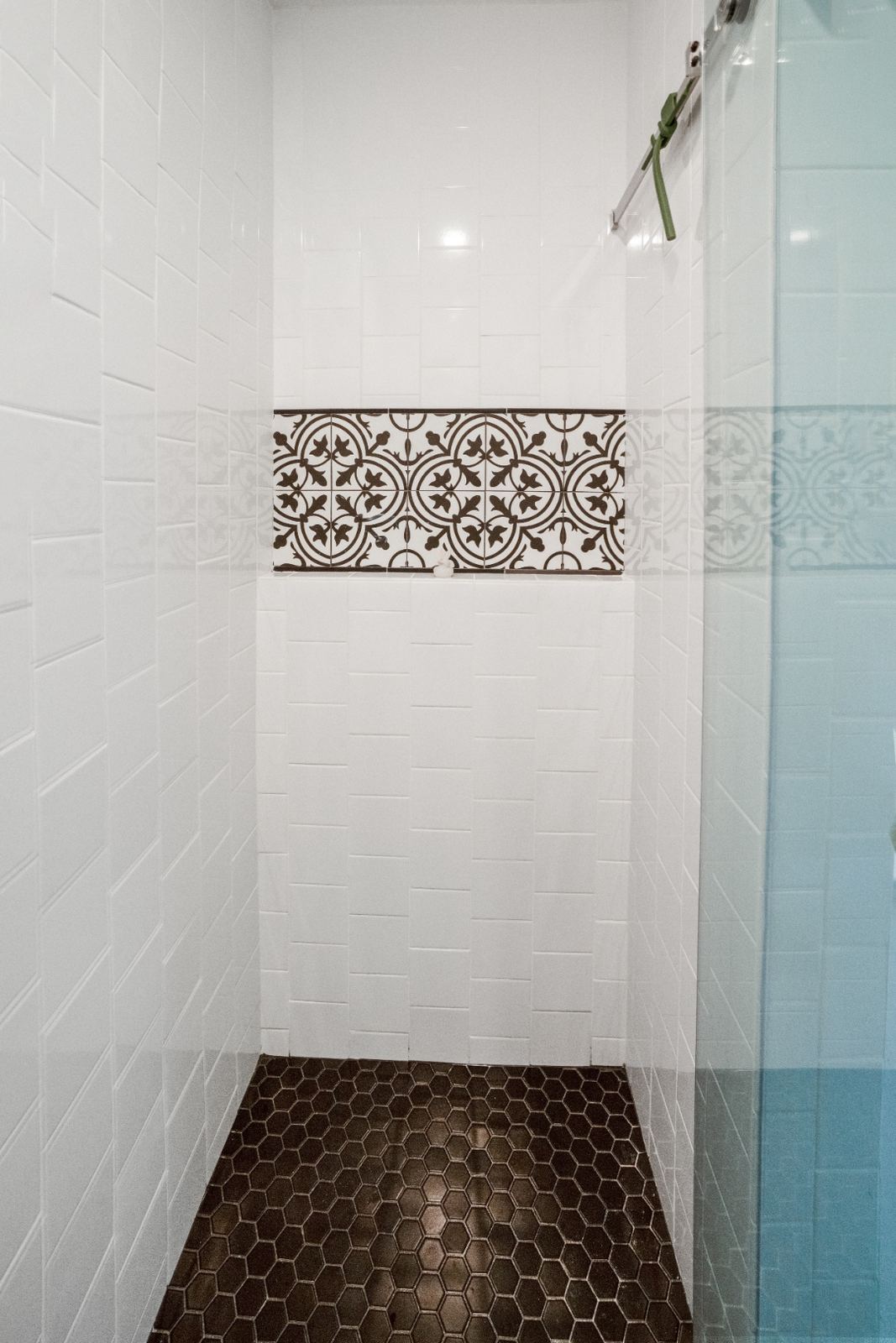 Shower interior with encaustic Victorian tile accent band and dark hex floor