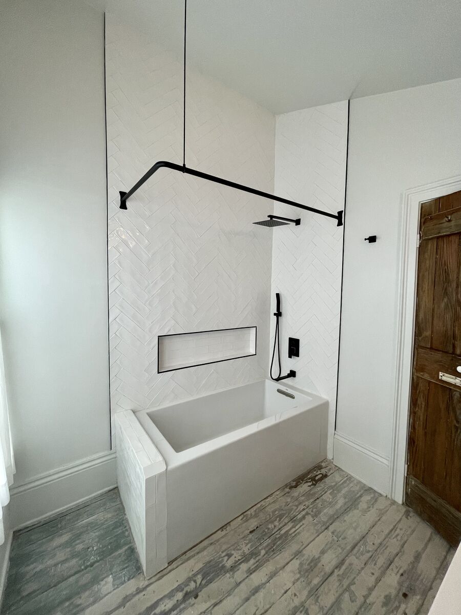 White herringbone tile tub surround with matte black square rain head, hand shower, and recessed niche
