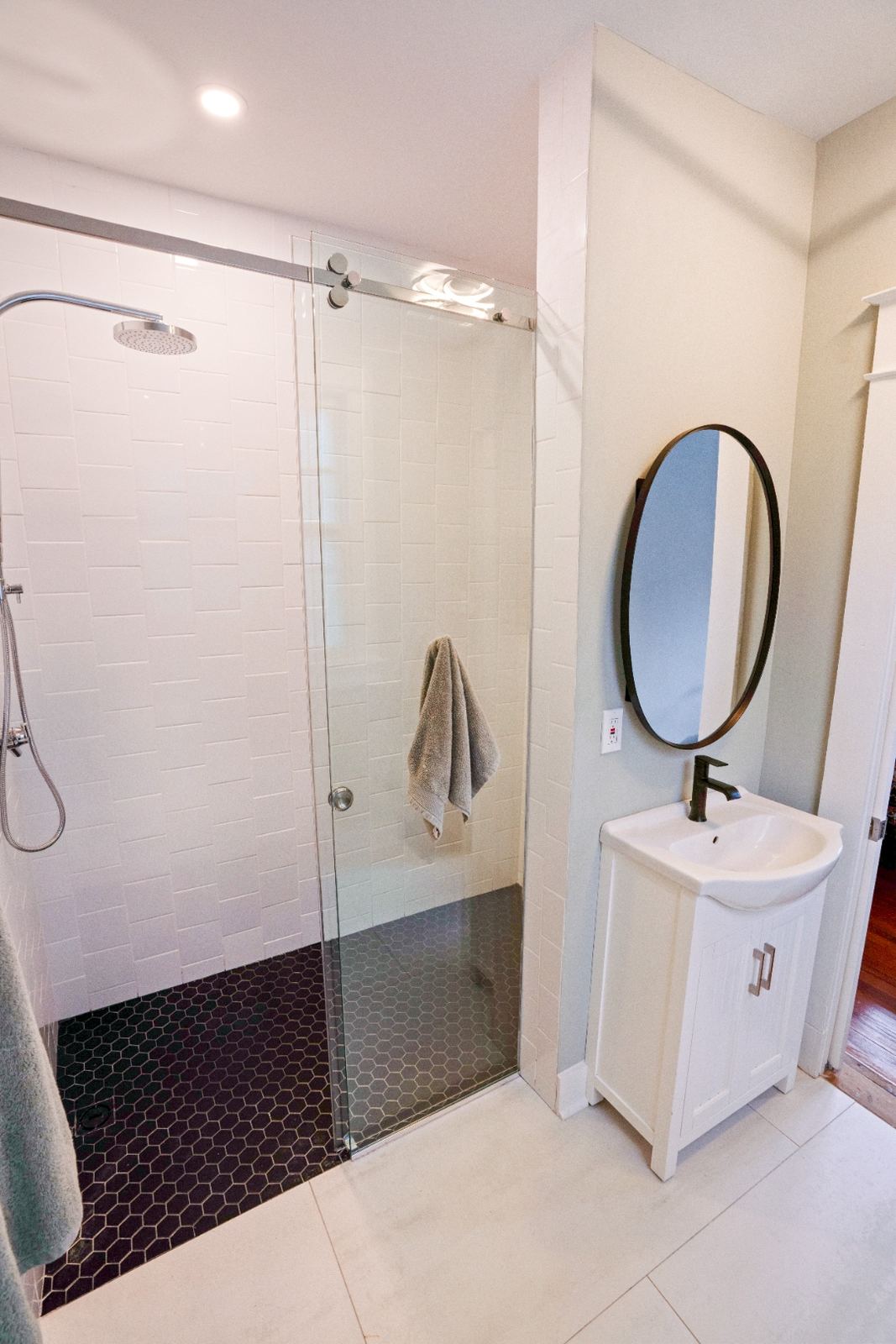 Custom subway tile shower with black hex floor and round mirror