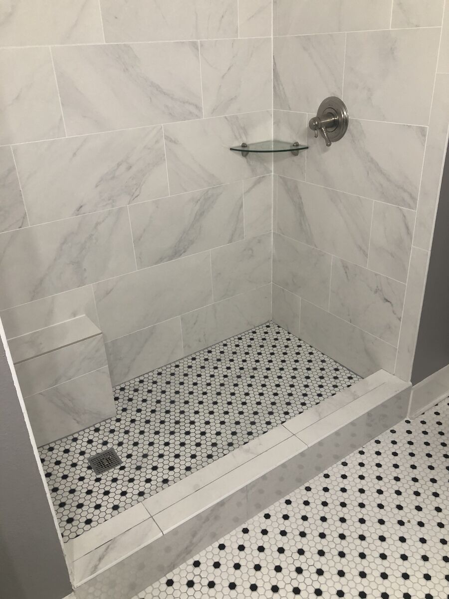 Marble tile walk-in shower with hex dot mosaic floor, corner glass shelf, and curb detail