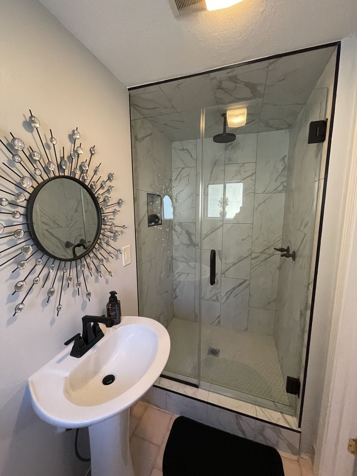 Marble shower with matte black fixtures and sunburst mirror