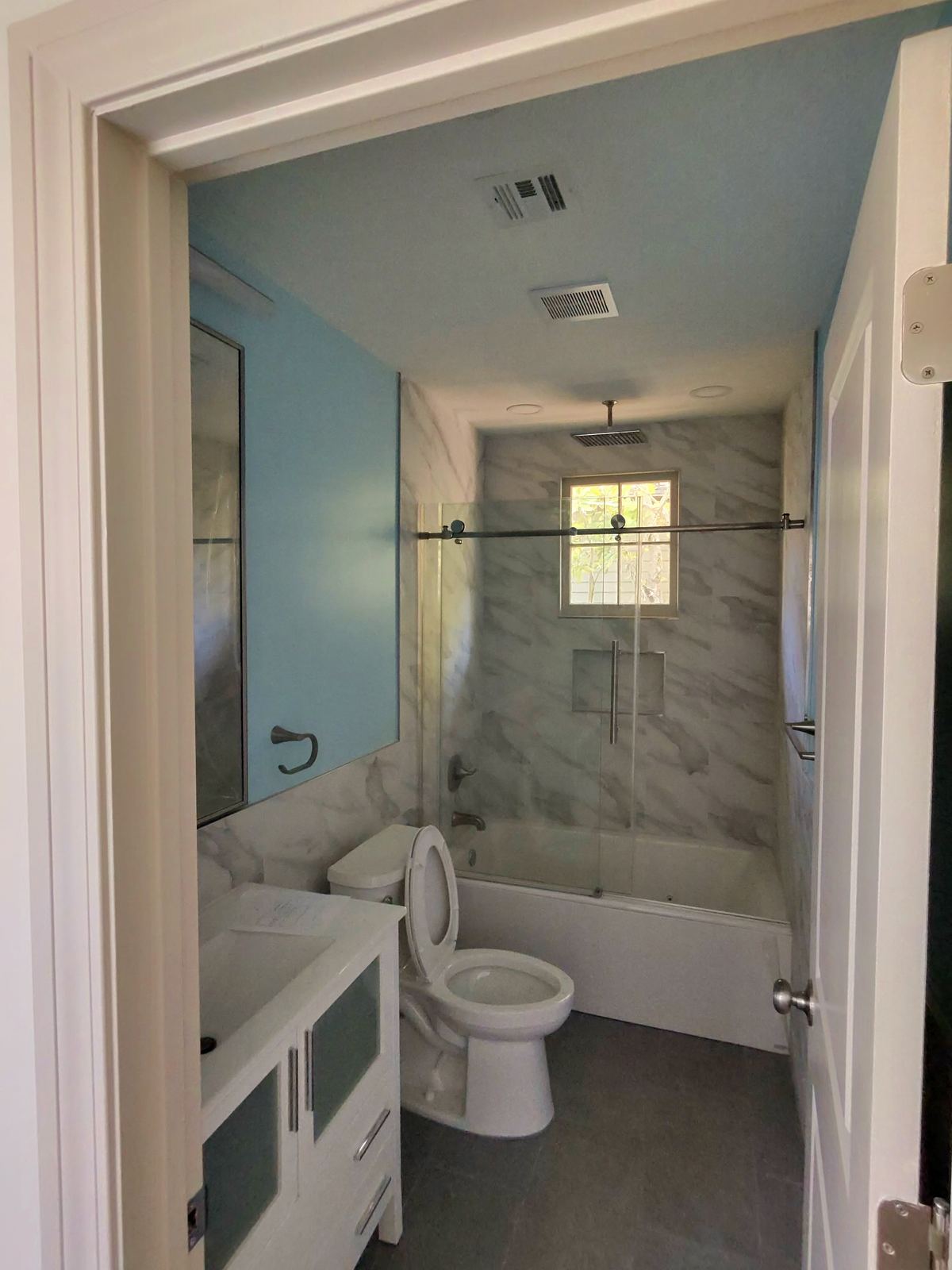 Marble tile tub and shower combo with blue walls and frameless glass enclosure