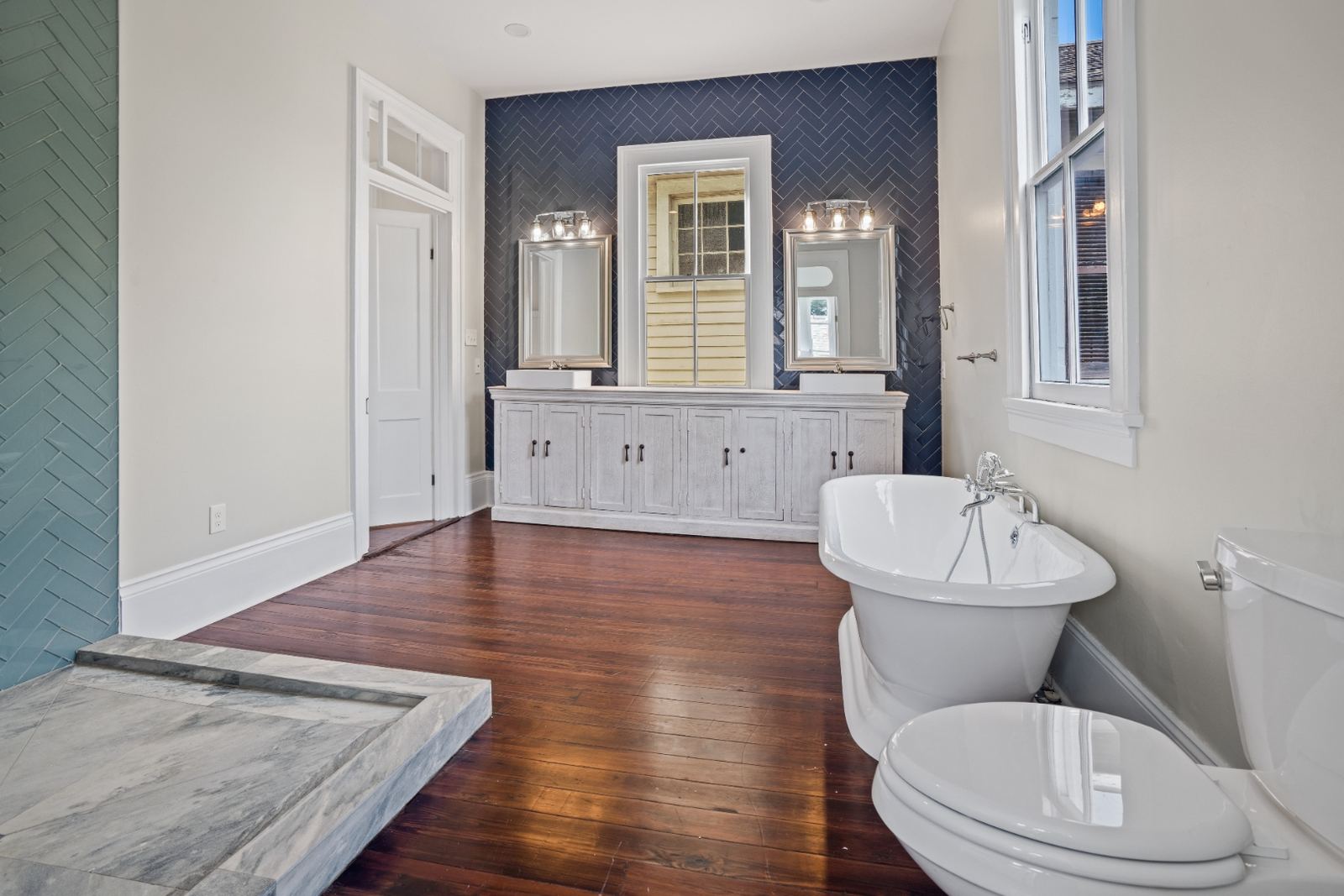 Navy herringbone accent wall with double vanity, freestanding tub and hardwood floors