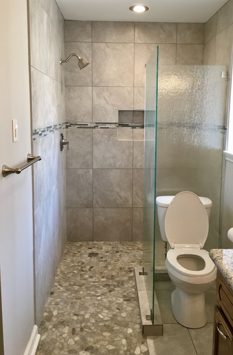 Walk-in shower with large format gray tile, pebble stone floor, mosaic accent band, and rain glass partition