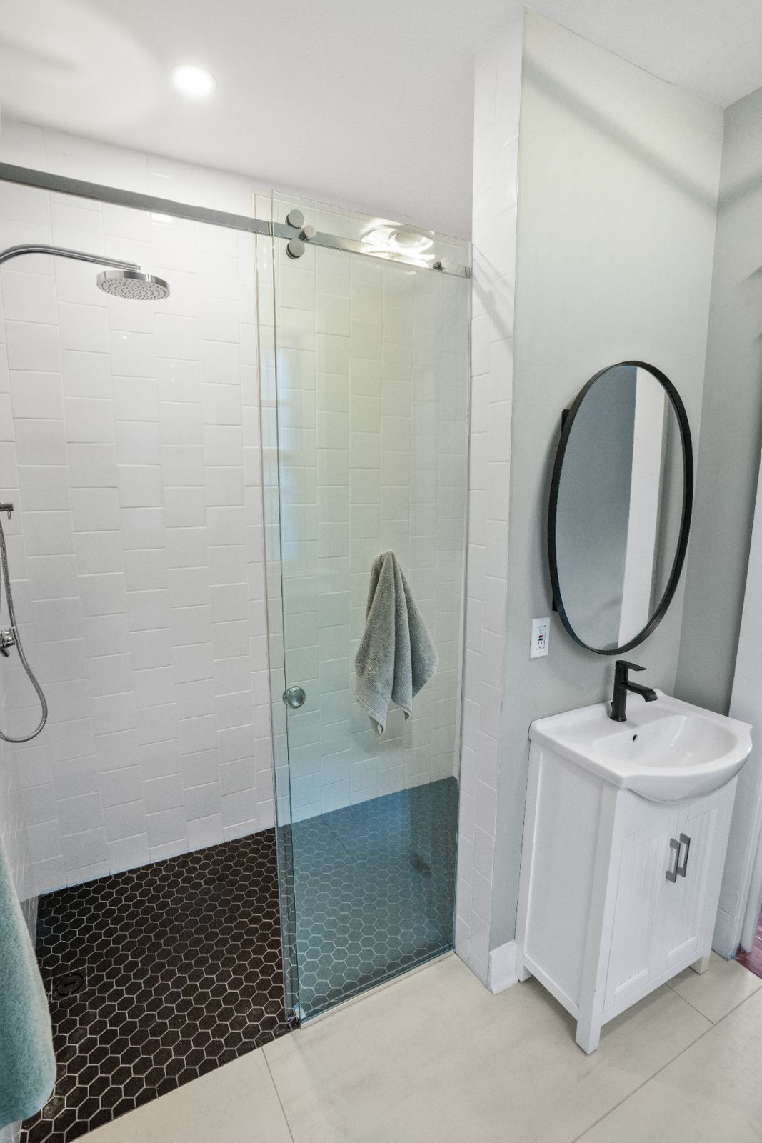 Shower with subway tile, dark hex floor and round black mirror vanity
