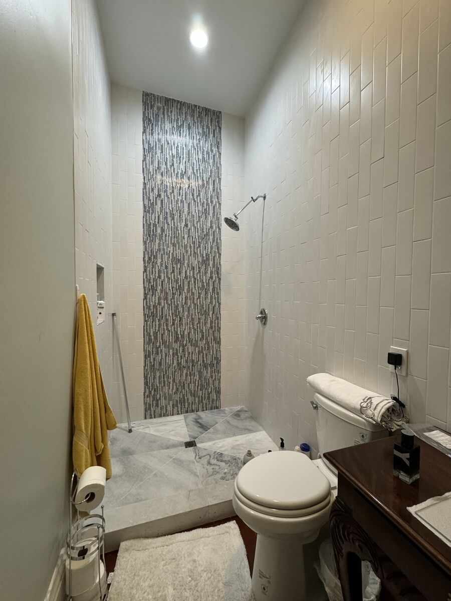 Clean white shower with brass curtain rod, brass towel bars, and natural light from transom window