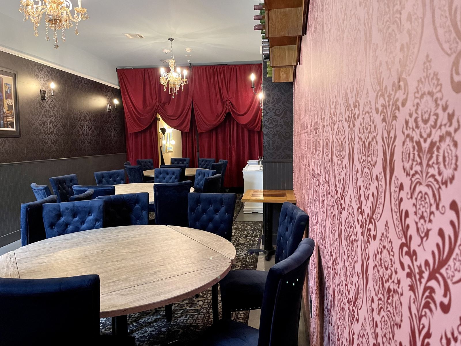 Upscale restaurant dining room with damask wallpaper, velvet navy chairs and gold chandeliers