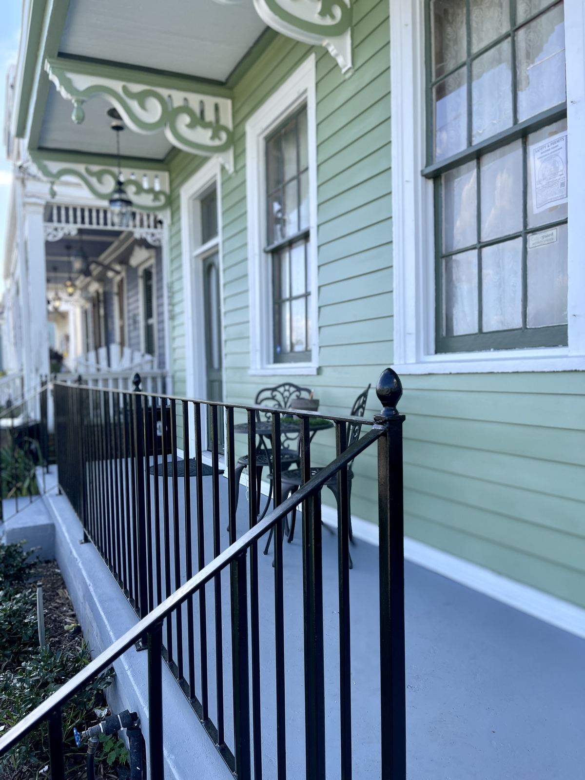 Completed green shotgun double restored porch with ornate bracketing and ironwork railing