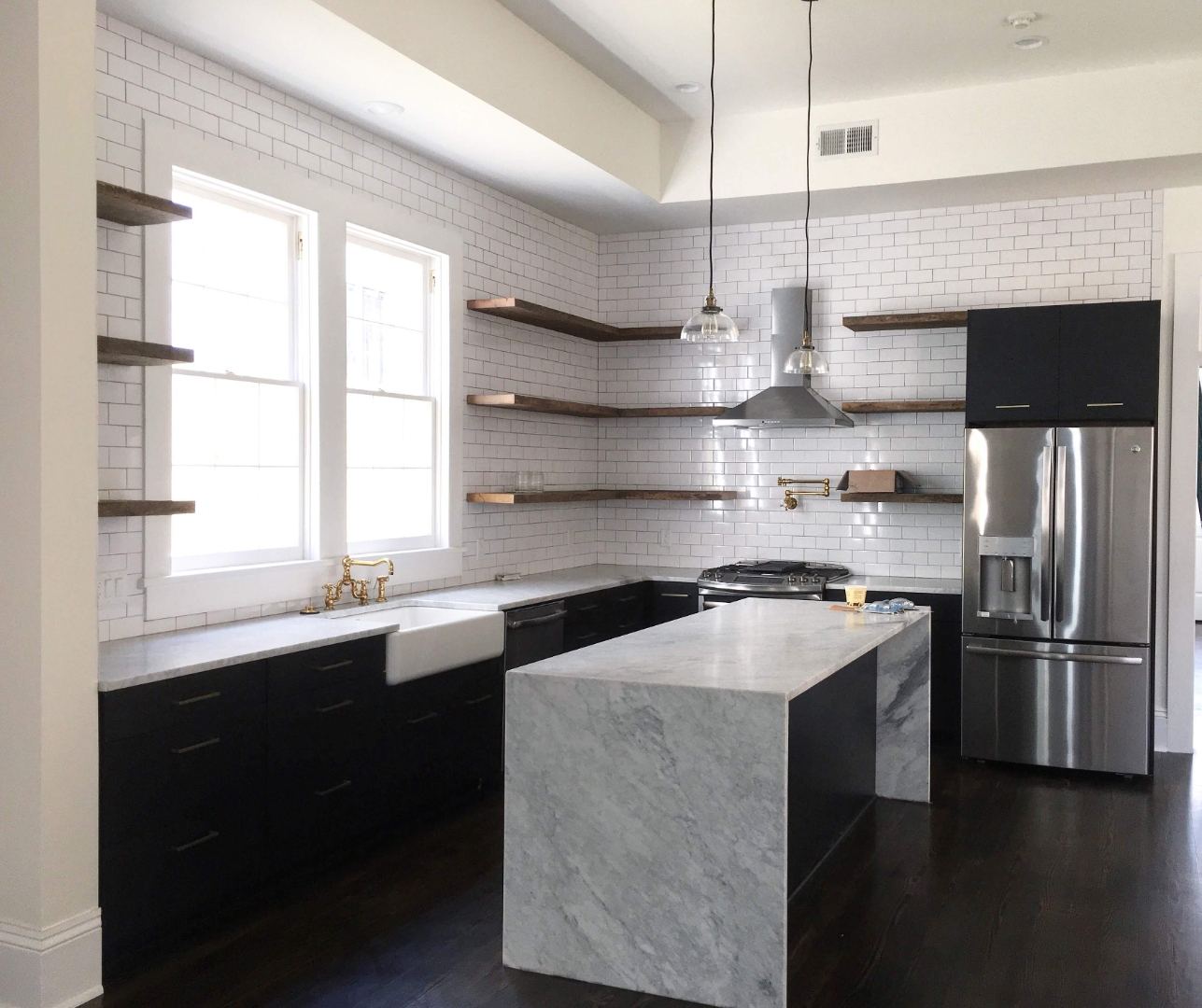 Black cabinet kitchen with marble waterfall island, subway tile and brass fixtures