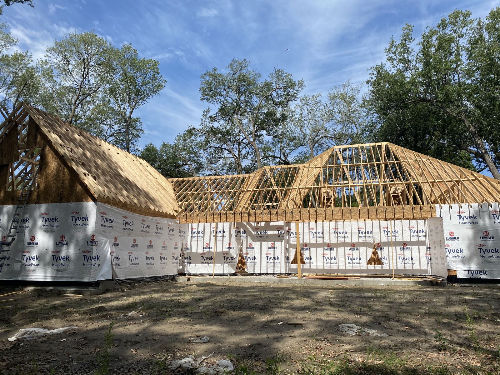 Custom home under construction with complex multi-gable roof framing under Louisiana live oaks
